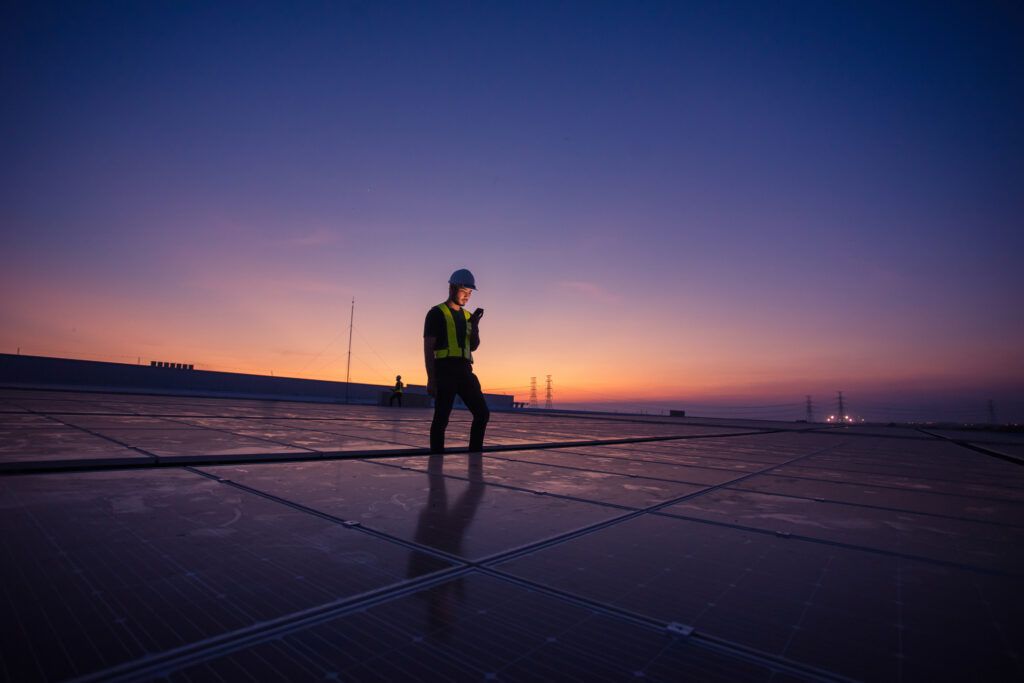 Lone worker standing in solar panel field at dusk holding tablet